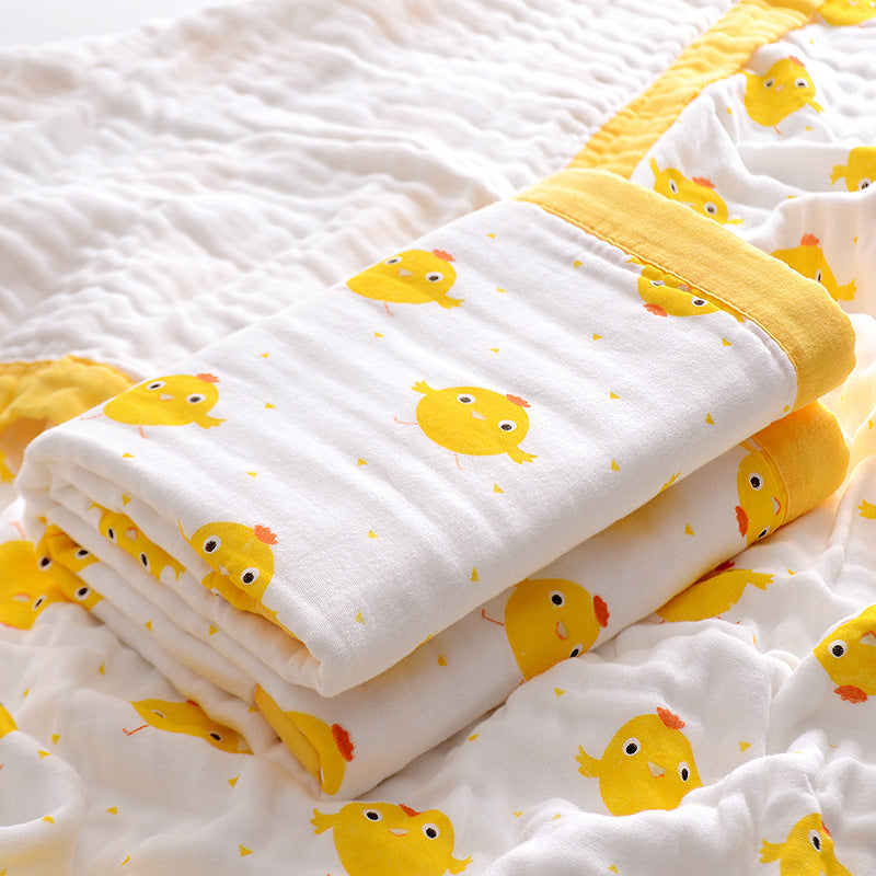  Folded 6-layer muslin cotton swaddle blanket with green trim and dinosaur print, laid on a matching muslin blanket