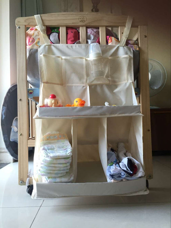 Beige hanging crib organizer mounted on a wooden crib storing toys and diapers