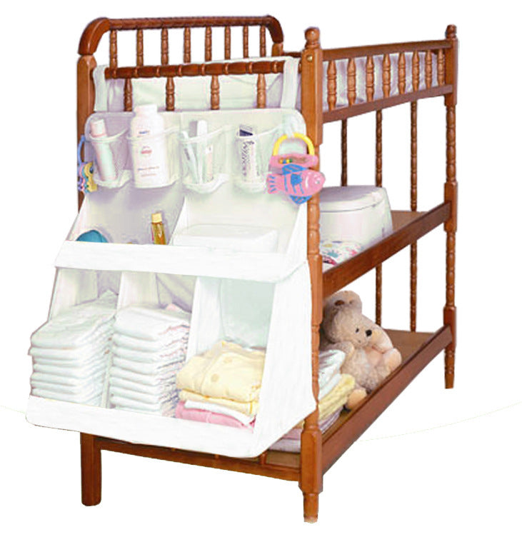 Hanging crib storage organizer with mesh pockets and diaper compartments on a wooden crib