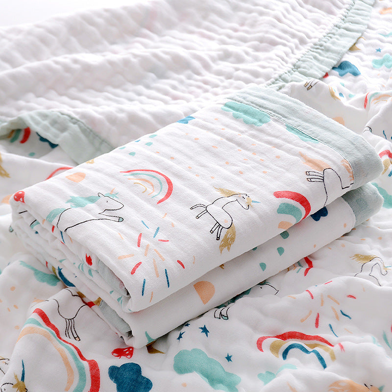  Folded 6-layer muslin cotton swaddle blanket with green trim and dinosaur print, laid on a matching muslin blanket