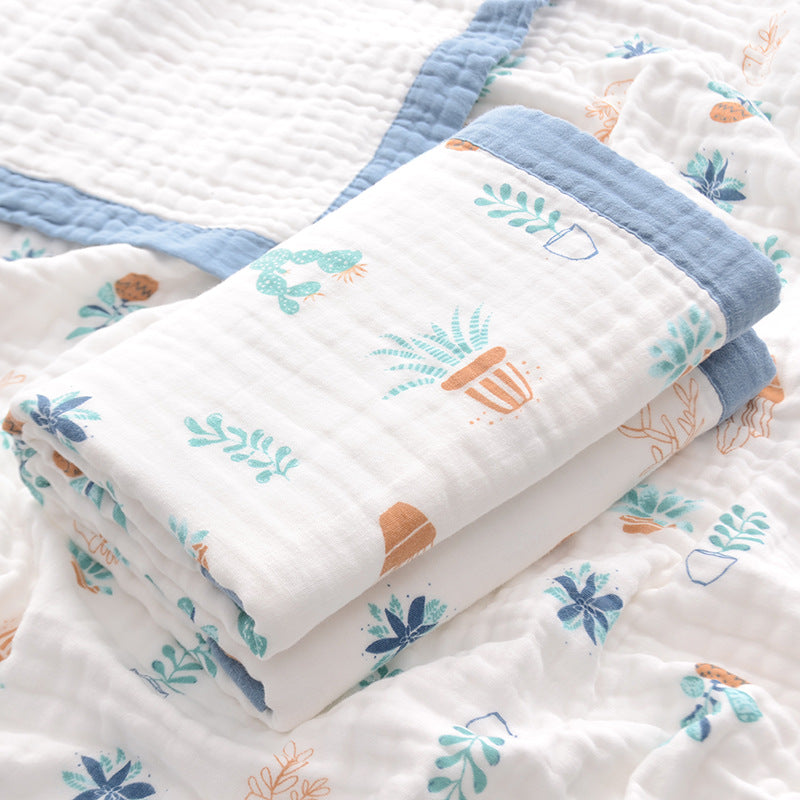  Folded 6-layer muslin cotton swaddle blanket with green trim and dinosaur print, laid on a matching muslin blanket